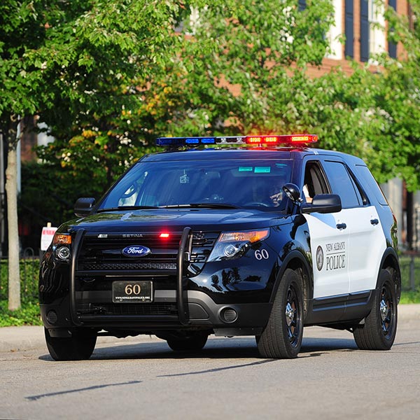 A New Albany Police SUV with flashing red and blue lights parked on a street with trees and buildings in the background.