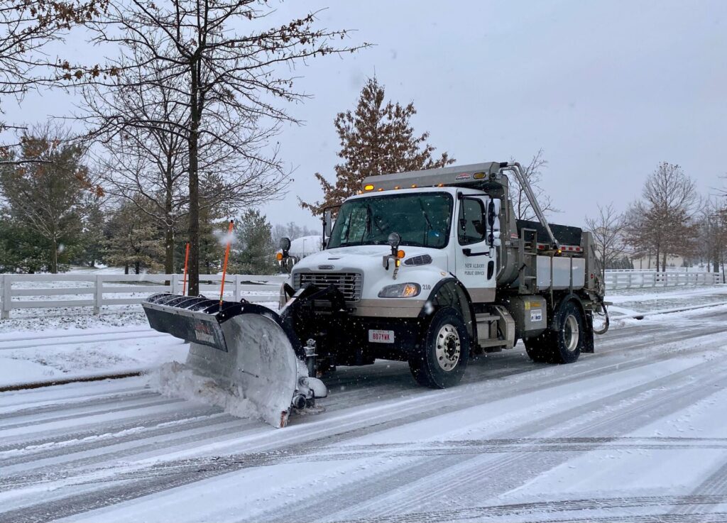 Front view of a snow plow driving down the street, actively moving snow.