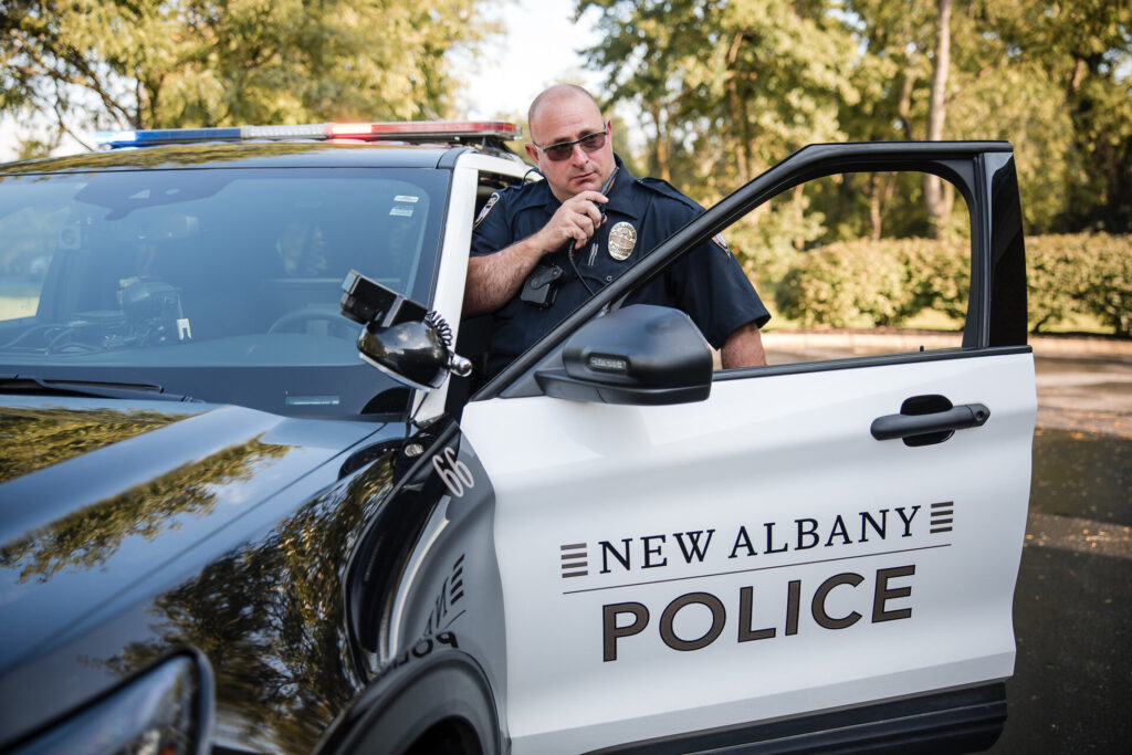 A New Albany police officer talking on the radio at his car