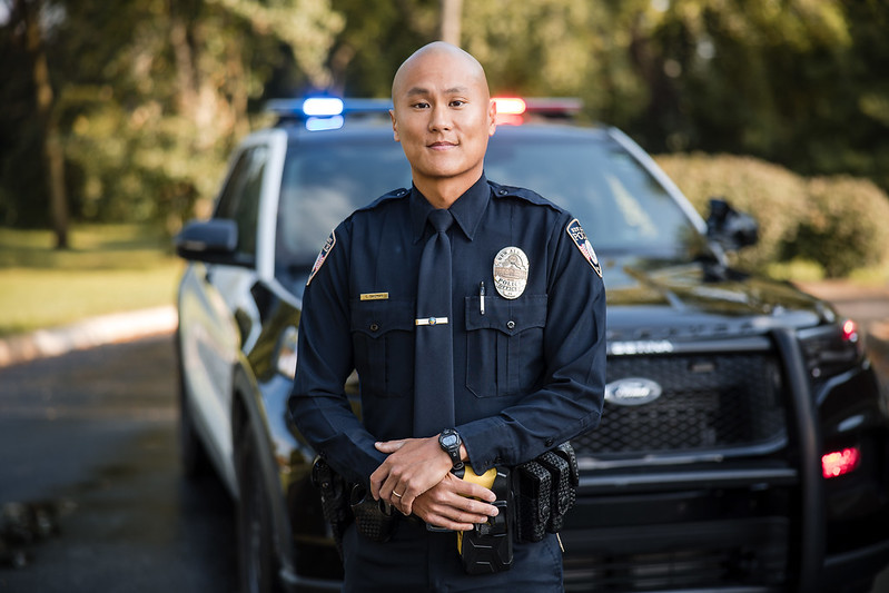 Police officer standing in front of a patrol vehicle with flashing lights.