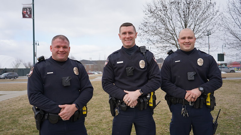 Three police officers in uniform standing and smiling outdoors.