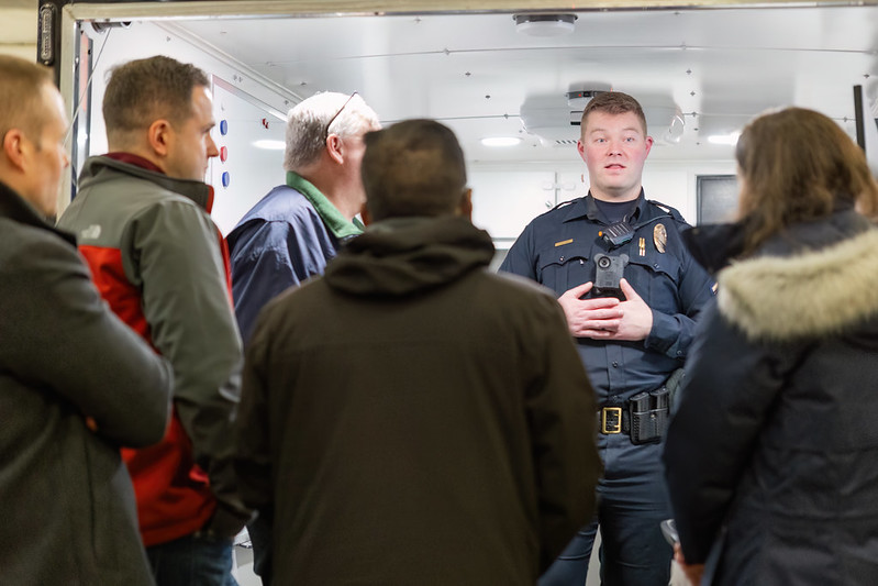 Police officer talking to a group of people in a room pod setting.