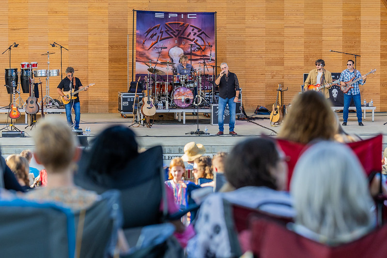 Band performing on an outdoor stage with musical instruments and equipment in front of an audience.