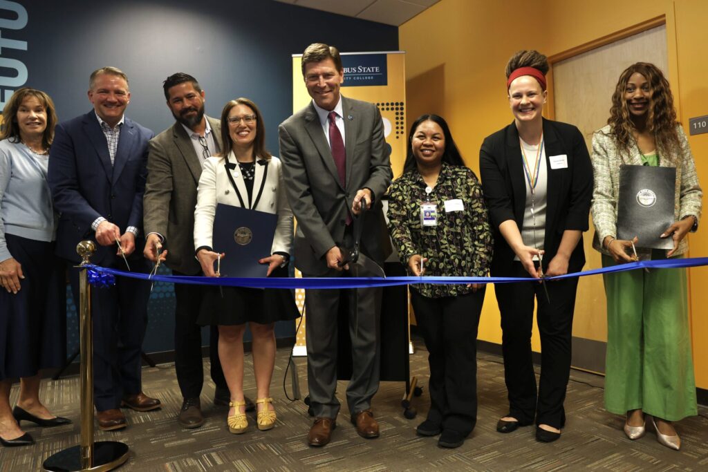 A group of people holding scissors and cutting a blue ribbon at a ceremonial event.