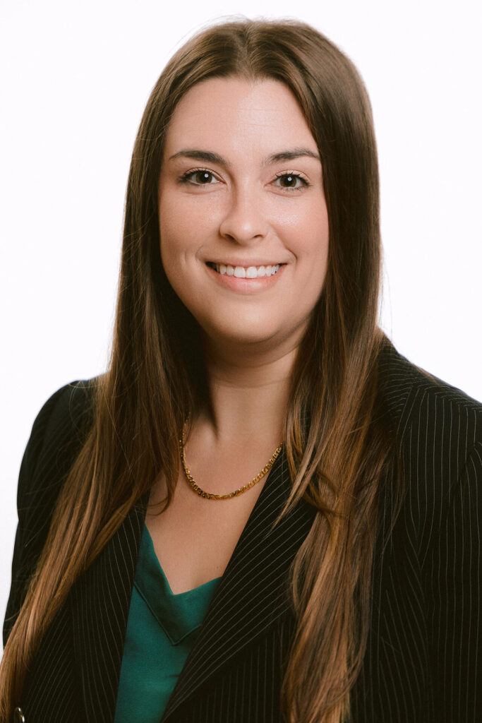 Portrait of a woman with long brown hair wearing a pinstripe blazer, green blouse, and a gold necklace.