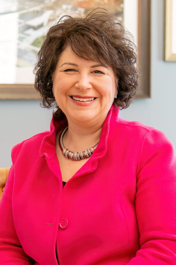 Smiling woman wearing a bright pink jacket and a silver necklace.