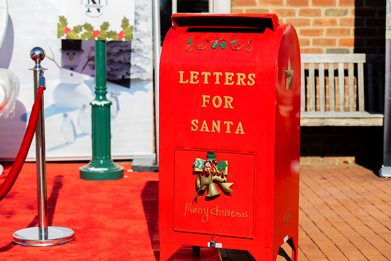 A red mailbox labeled "Letters for Santa" on a red carpet, surrounded by holiday decorations.