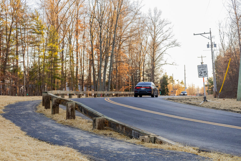 Car driving on a rural road with a speed limit sign of 25 mph, surrounded by bare trees.