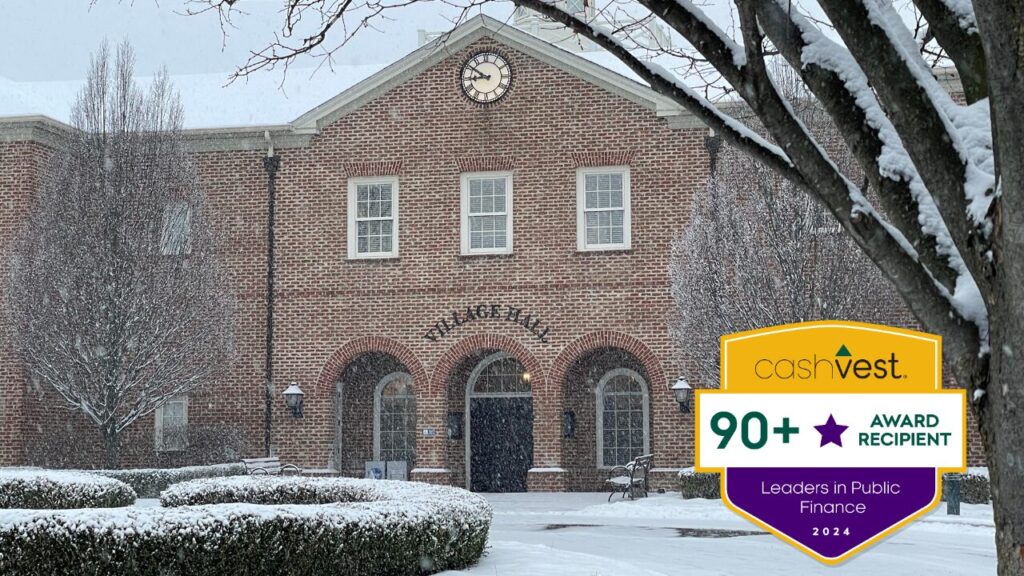 Brick building labeled "Village Hall" in winter with snow on the ground, trees, and roof; a badge on the image says "cashVest 90+ Award Recipient Leaders in Public Finance 2024."