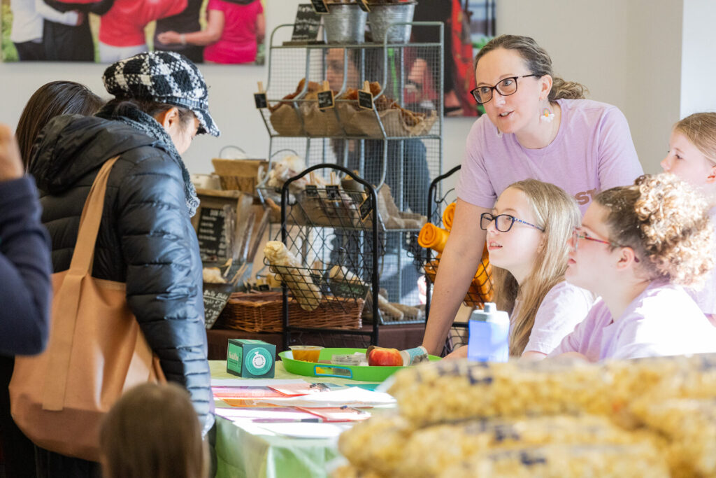 A group of people interacting at a market table with various goods on display.