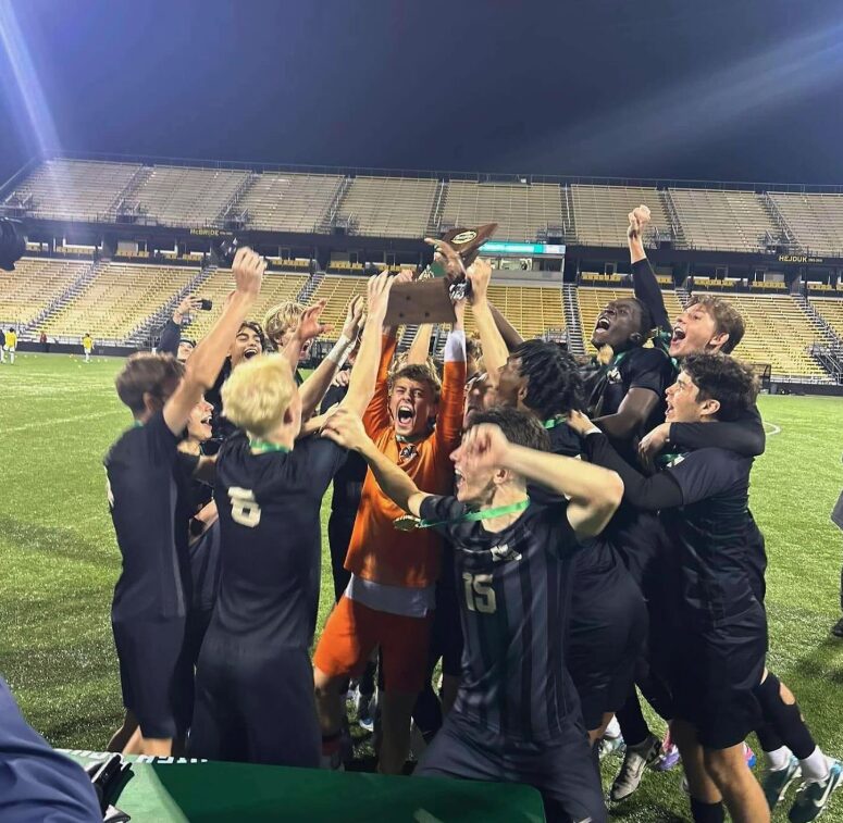 Soccer team celebrating with a trophy on a stadium field at night.