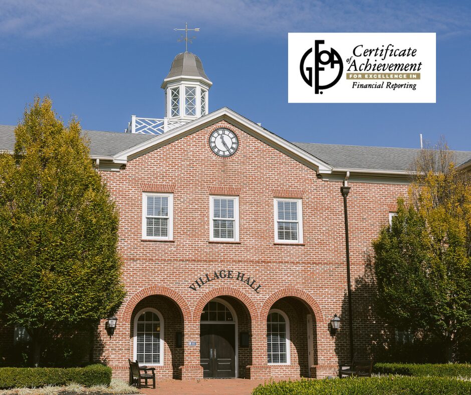 A brick Village Hall building with arched doorways and a clock on the gable, flanked by trees, with a certificate label for excellence in financial reporting in the top right corner.