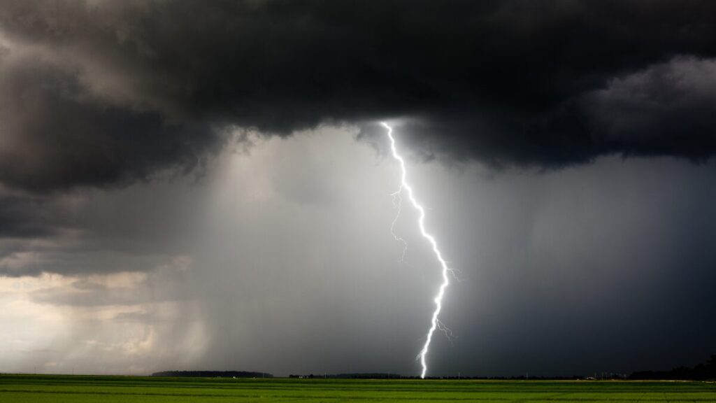 A bolt of lightning striking a green field under a sky filled with dark, stormy clouds.