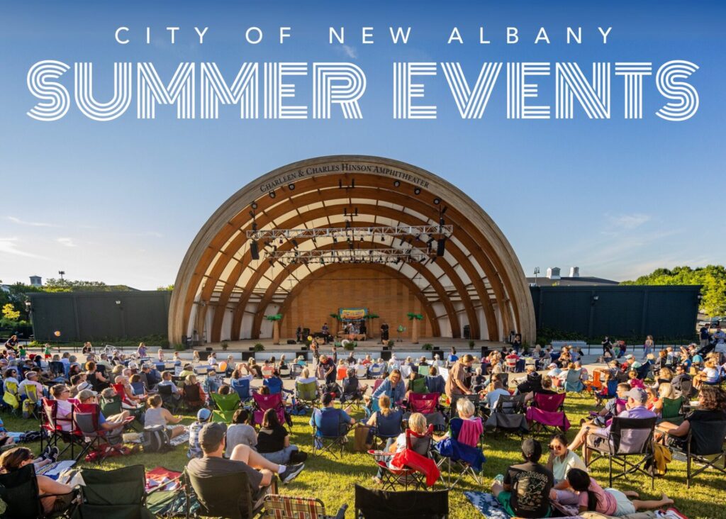 Outdoor summer event at the Charleen & Charles Hinson Amphitheater in New Albany with a crowd seated on grass and folding chairs facing a wooden stage under a clear blue sky.