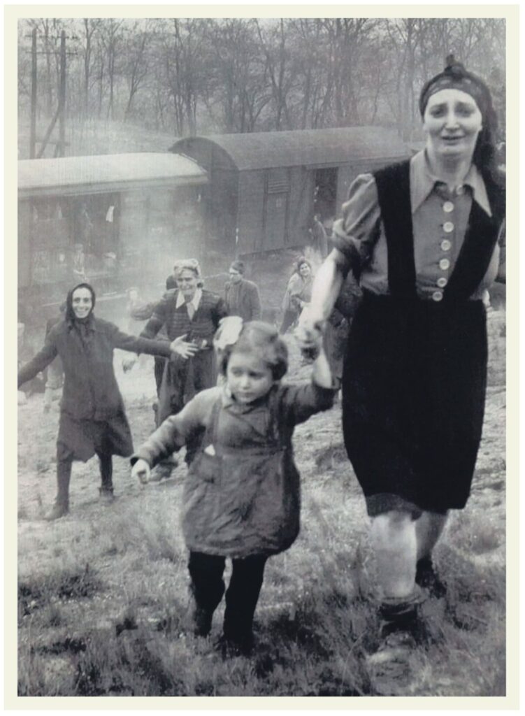 Black and white photo of a group of people, including women and children, walking uphill away from a train in a rural, wooded area, with one woman holding a child's hand in the foreground.