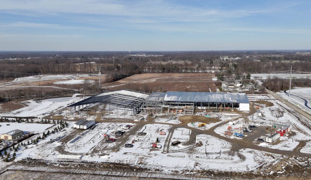 Aerial view of a large metal-framed building under construction in snow-covered fields with construction vehicles
