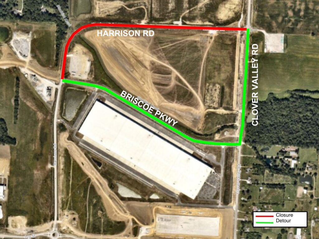 Aerial satellite map showing a large white-roofed warehouse site with a road closure highlighted in red along Harrison Road across the top and a green detour route following Briscoe Parkway and Clover Valley Road, with a small legend labeling red as Closure and green as Detour.