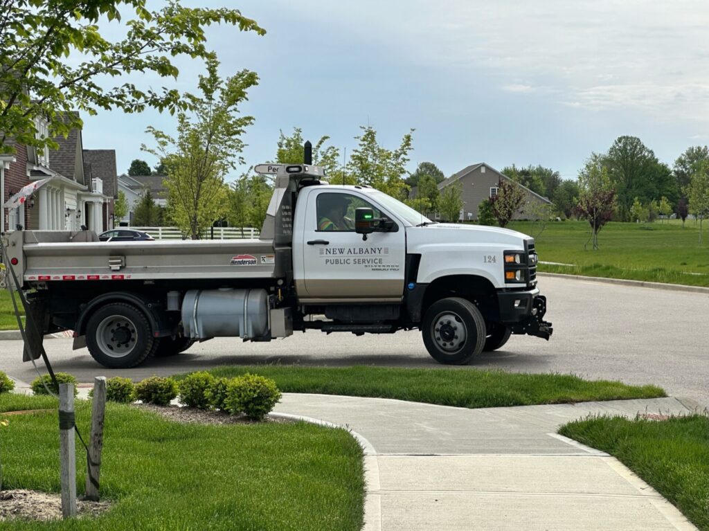 White New Albany Public Service dump truck (unit 124) parked on a suburban street beside sidewalks and lawns.