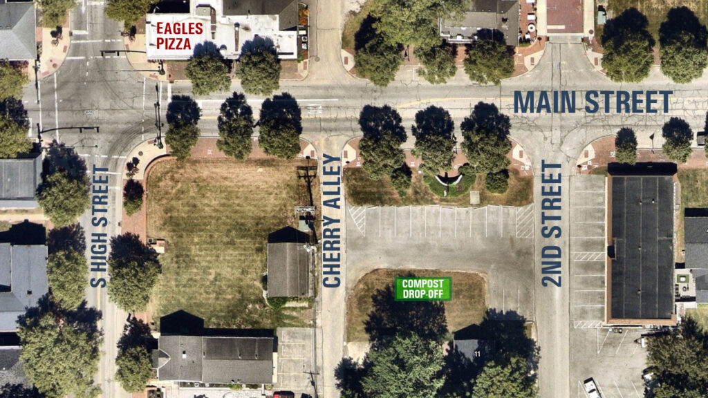 Aerial view of a town square showing labeled streets (Main, 2nd, S High, Cherry Alley), trees, parking lots, and a "Compost Drop-Off" sign.