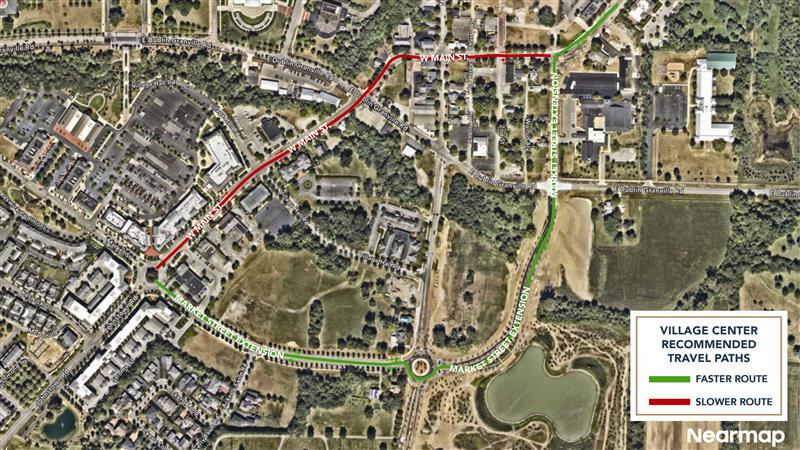 Aerial map of a village center showing recommended travel paths: green line for faster route, red line for slower route, roads and roundabout.