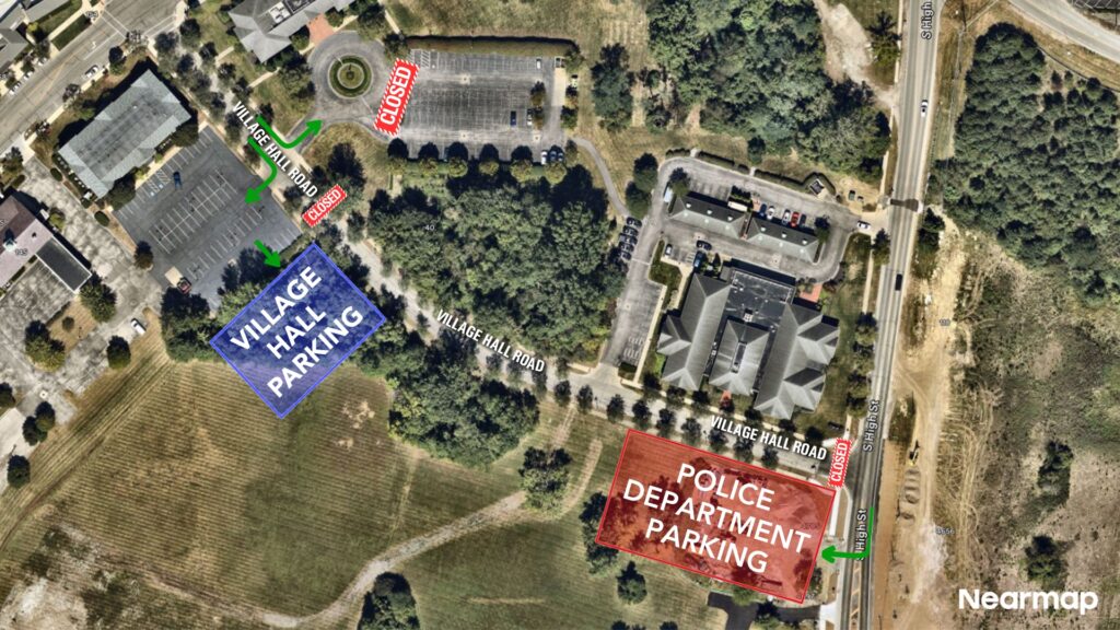 Aerial map showing Village Hall Parking area marked in blue at left and Police Department Parking marked in red at right, with labeled Village Hall Road, closed signs, arrows indicating routes, surrounding buildings and trees.