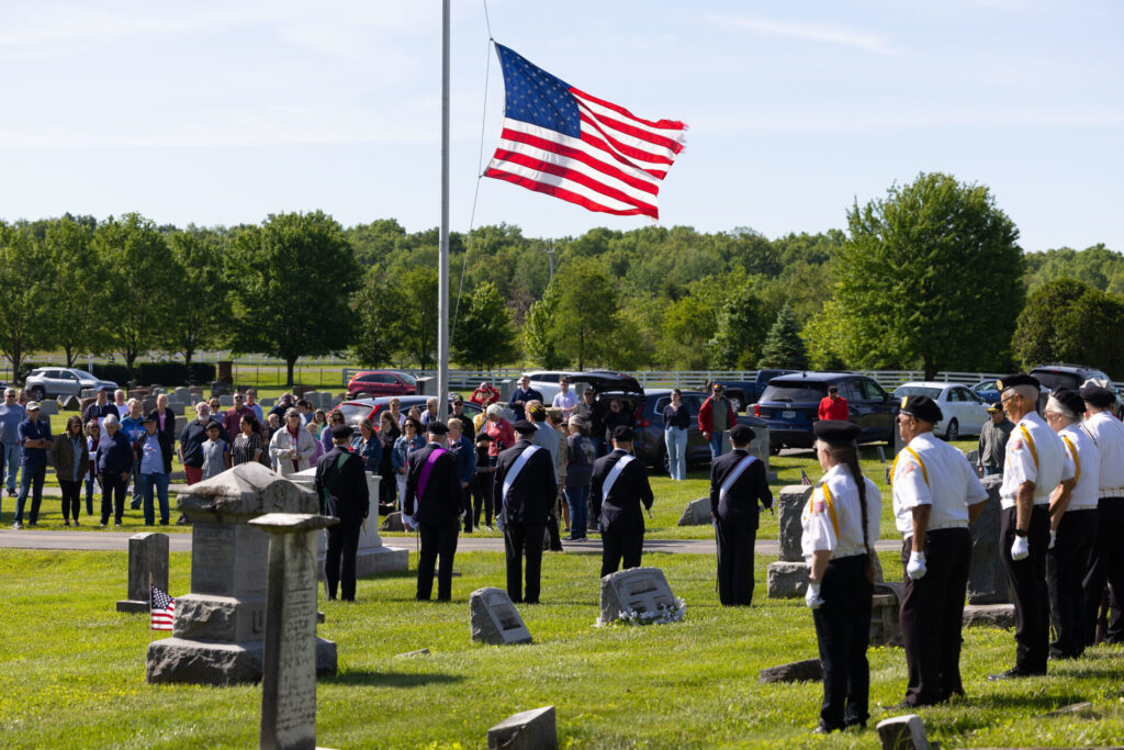 Memorial Day Ceremony attendees gather around a US flag at half mast