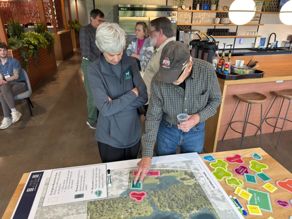 Couple examining a large map on a table in a bright café-style meeting space, colorful labels and markers scattered nearby.