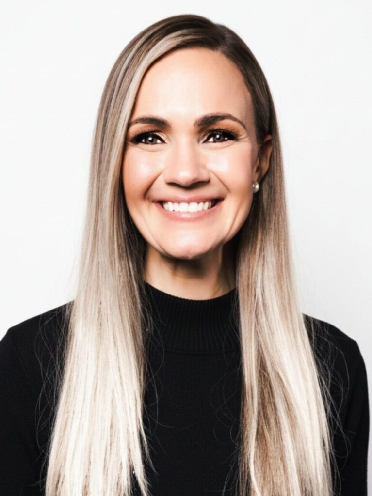 Smiling woman with long straight blonde hair wearing a black turtleneck against a white background