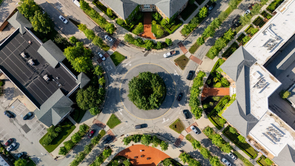 Aerial view of a tree-filled circular roundabout surrounded by buildings, sidewalks, parked cars, and landscaped greenery
