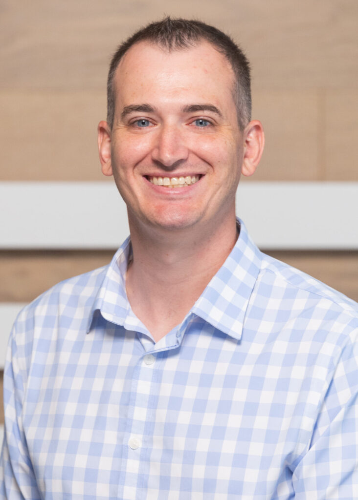 Konner Barr smiles for a headshot photo. He is wearing a blue and white patterned shirt.