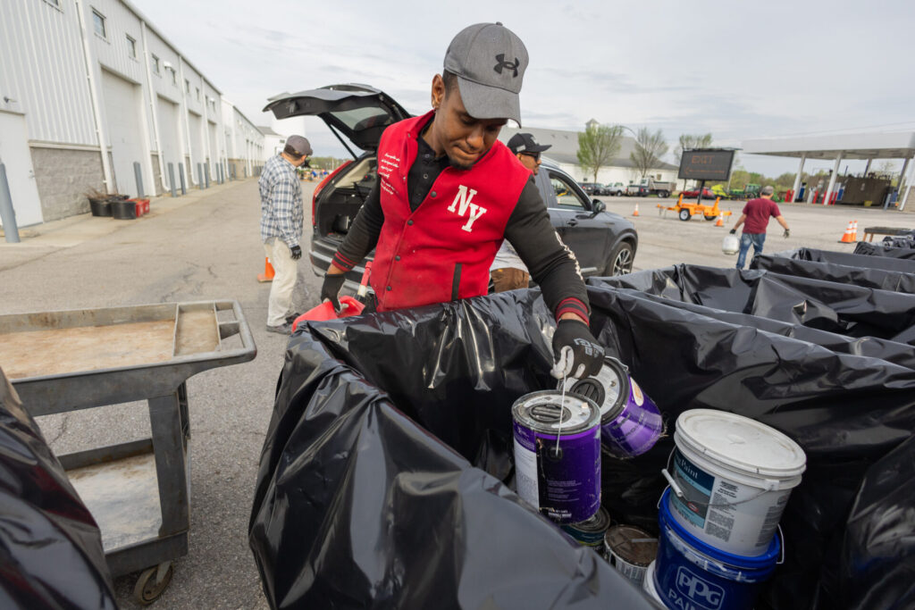 A man in a red jacket puts old paint cans in a bin.