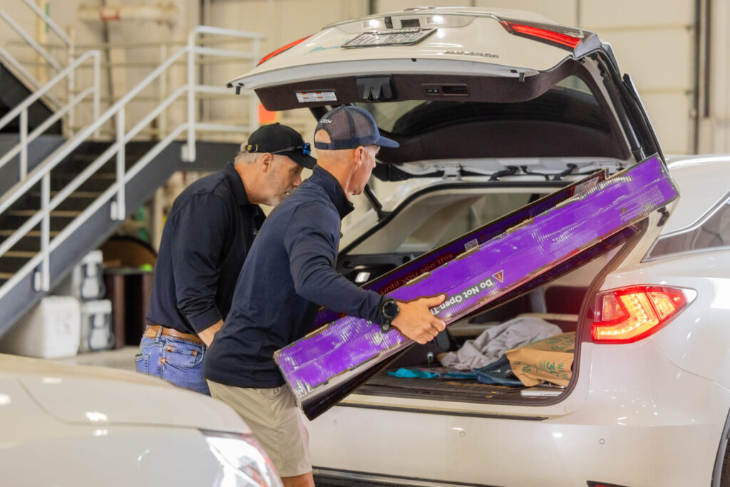 Two men are pulling an old tv out of a trunk of a car.